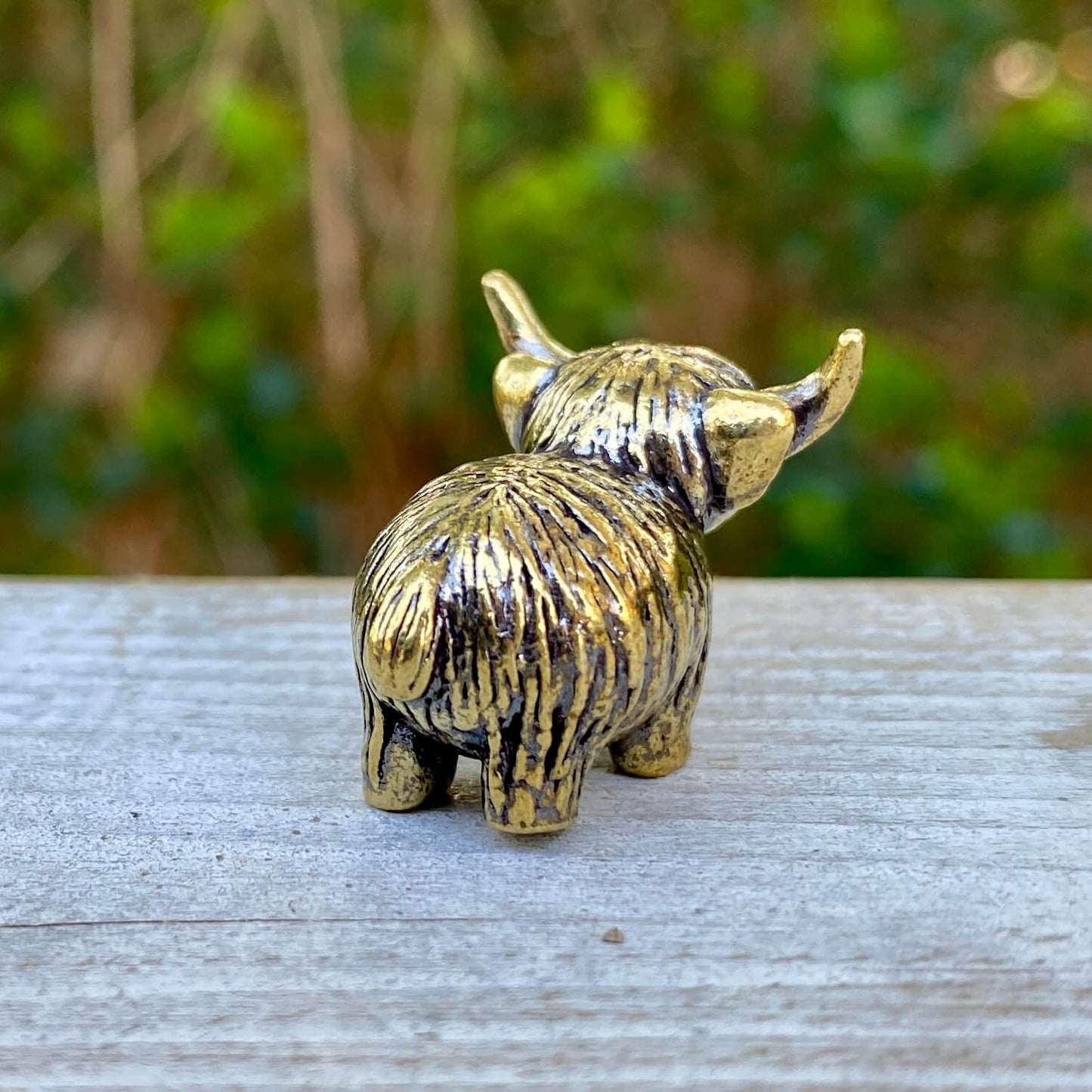 Solid brass tiny Highland mini cow figurine by Wild Brass, symbol of joy, charm, and contentment, shown in close-up detail.