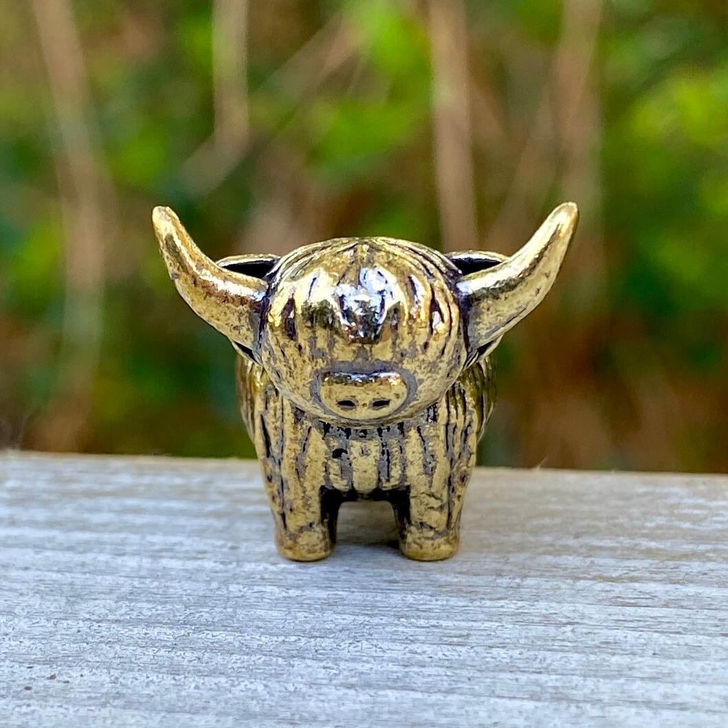 Solid brass tiny Highland mini cow figurine by Wild Brass, symbol of joy, charm, and contentment, shown in a close-up image.